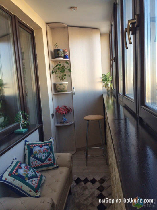 Уютный балкон с коричневыми рамами, шкафом и местом для отдыха с диваном