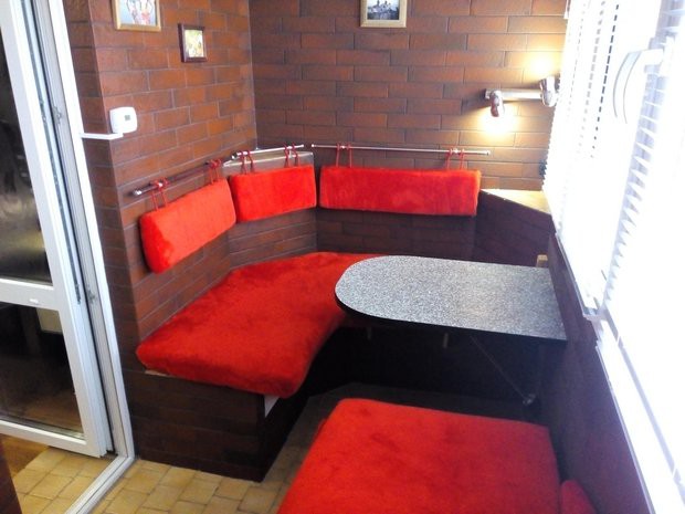 Балкон с красным угловым диваном и стенами под кирпич