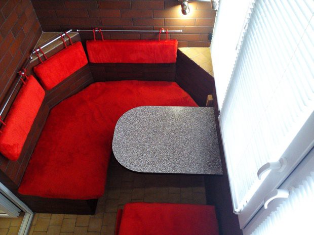 Балкон с красным угловым диваном и стенами под кирпич